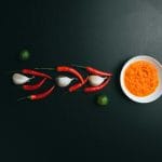 stock photo of some chilis, garlic cloves, limes, and a bowl of red sauce arranged artistically on a black background